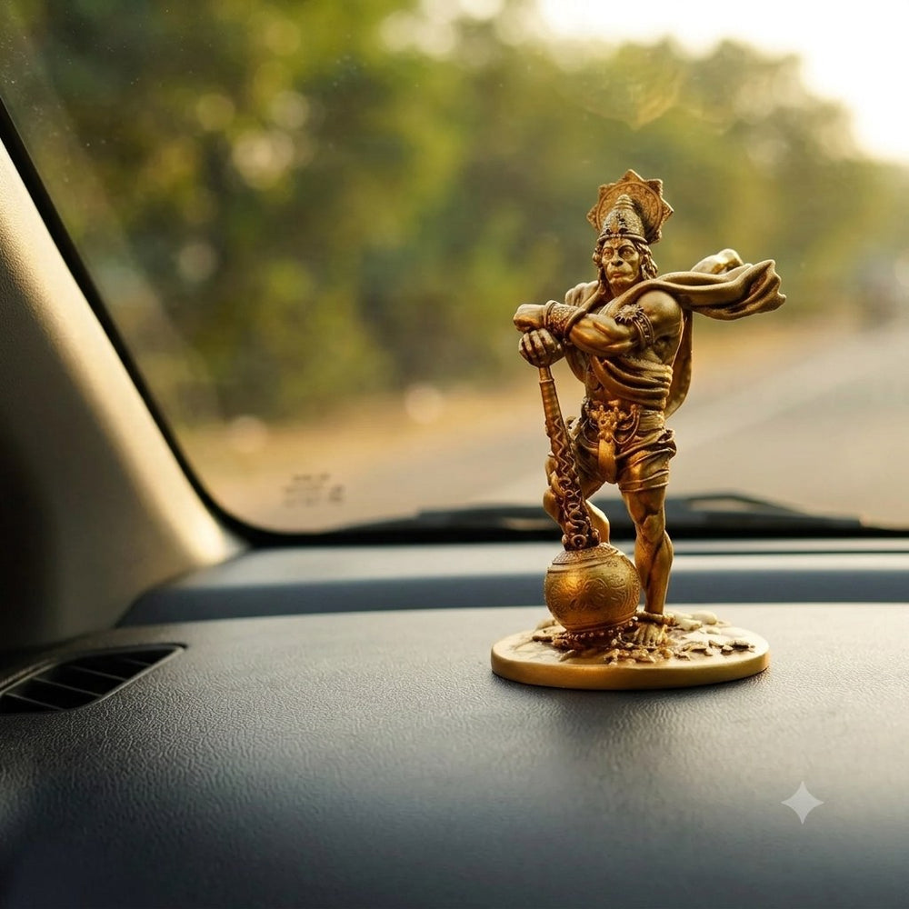 Bahubali Hanuman idol in antique gold on a car dashboard, with the road visible through the windscreen